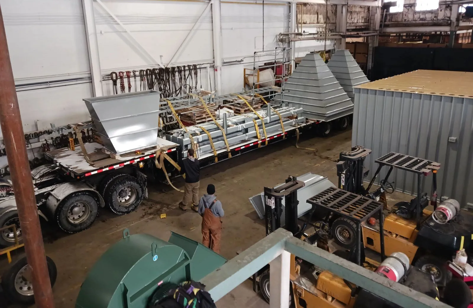 Steel parts and hoppers strapped down on a flatbed trailer inside a plant