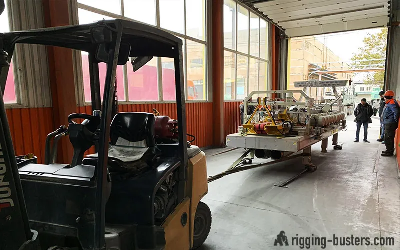 Forklift loading a machine onto a trailer inside a plant