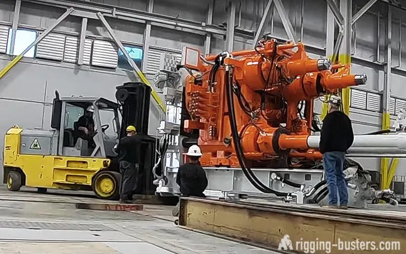 Crew moving a large industrial machine on steel cribbing with a heavy-capacity forklift