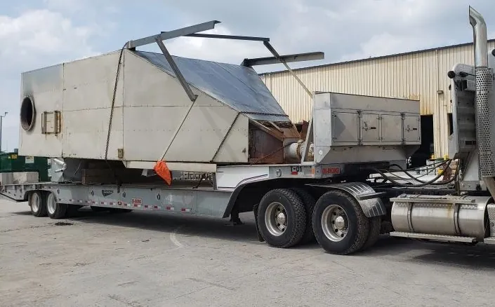 Large industrial enclosure loaded on a step-deck trailer behind a tractor