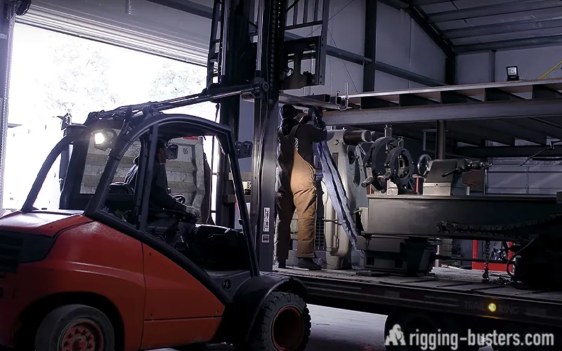 Forklift loading a machine onto a trailer in a warehouse