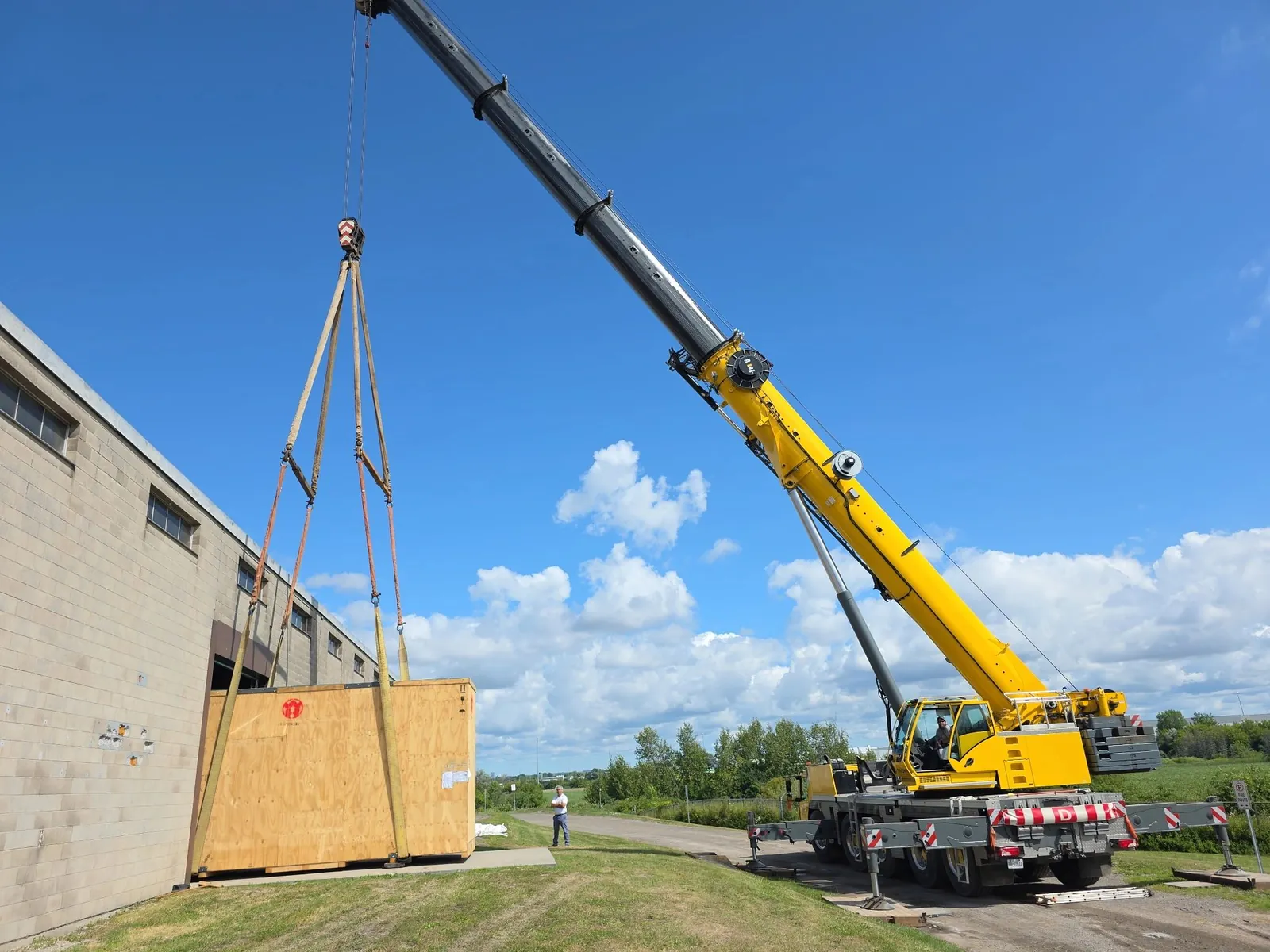 Mobile crane lifting a crated machine next to an industrial building