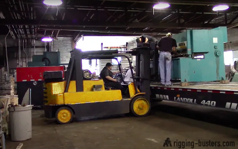 Forklift loading a press brake onto a tilt-deck trailer